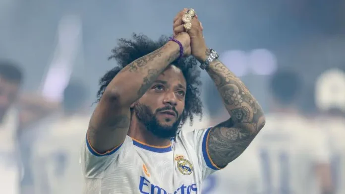 Marcelo, ex-lateral do Real Madrid e da Seleção Brasileira, sorri enquanto segura uma taça, simbolizando sua vitoriosa carreira repleta de conquistas e momentos inesquecíveis no futebol